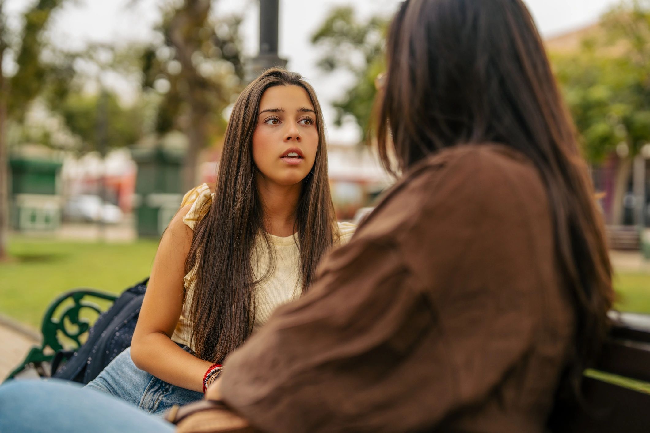 Teenage girl in conversation with an adult on a park bench